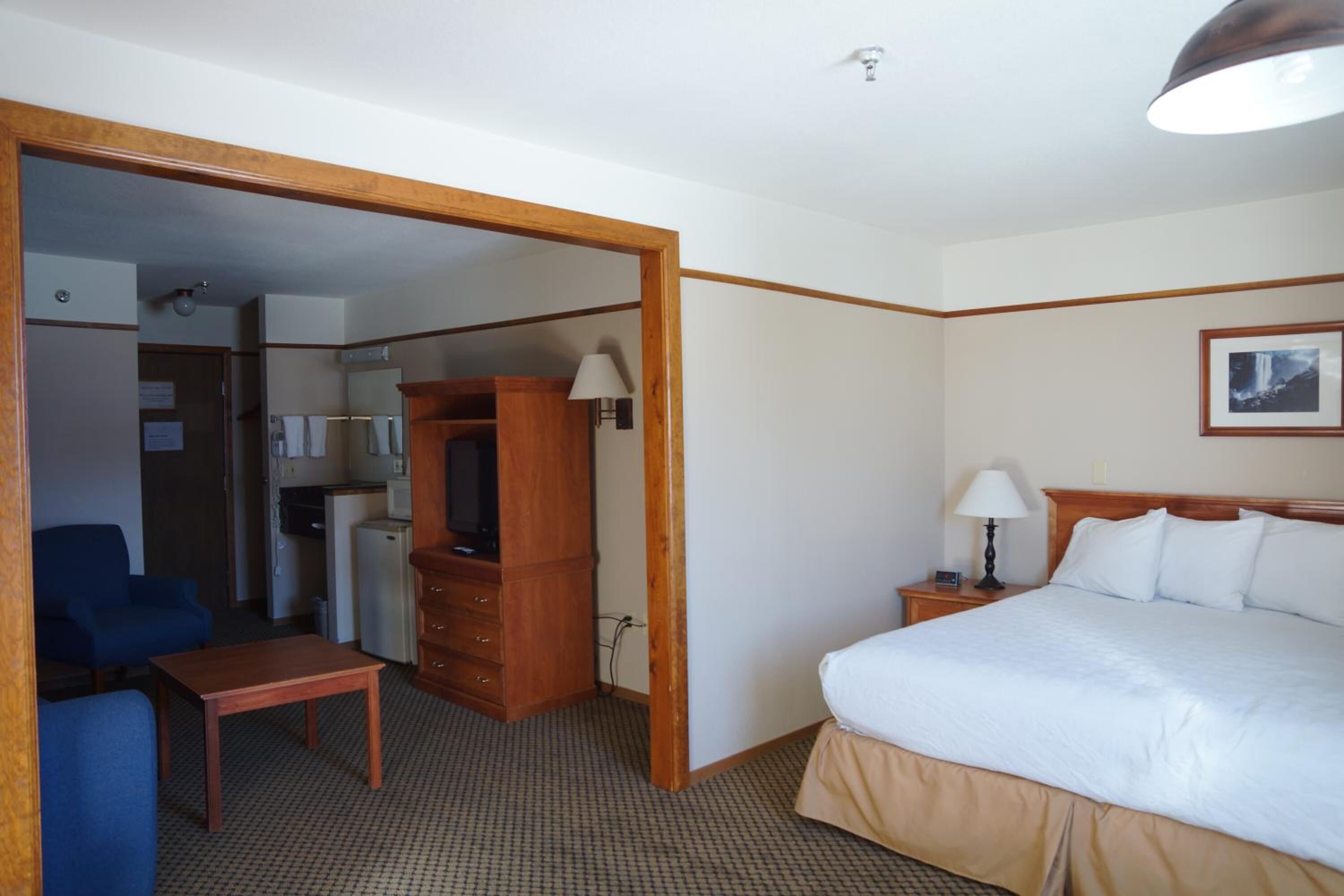 A hotel room with a bed, a desk, a chair, a wardrobe, a nightstand, and a lamp.