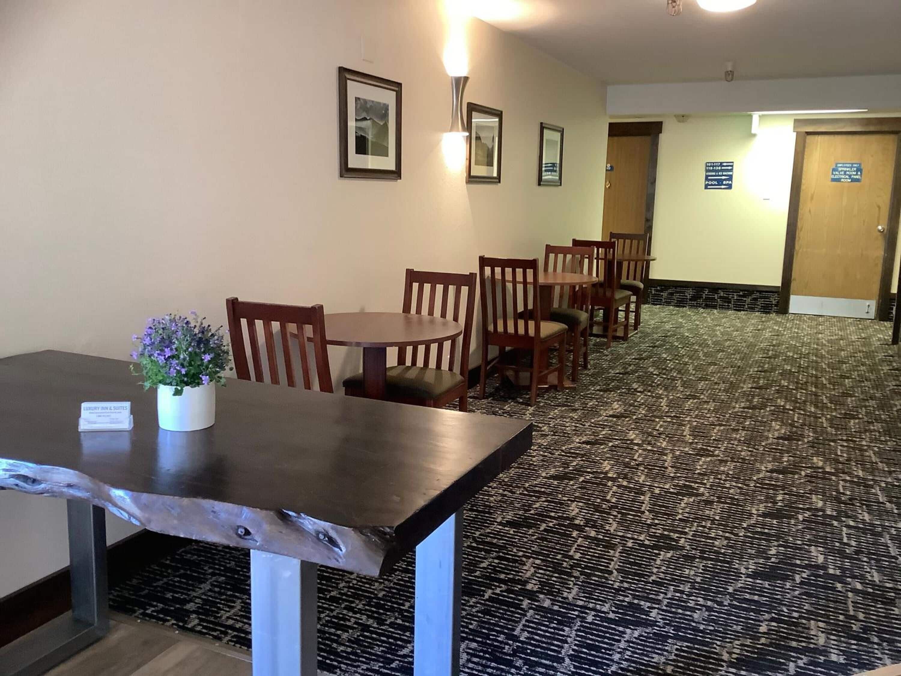 Un comedor de hotel con una mesa larga y sillas, una planta pequeña en maceta y cuadros en la pared.