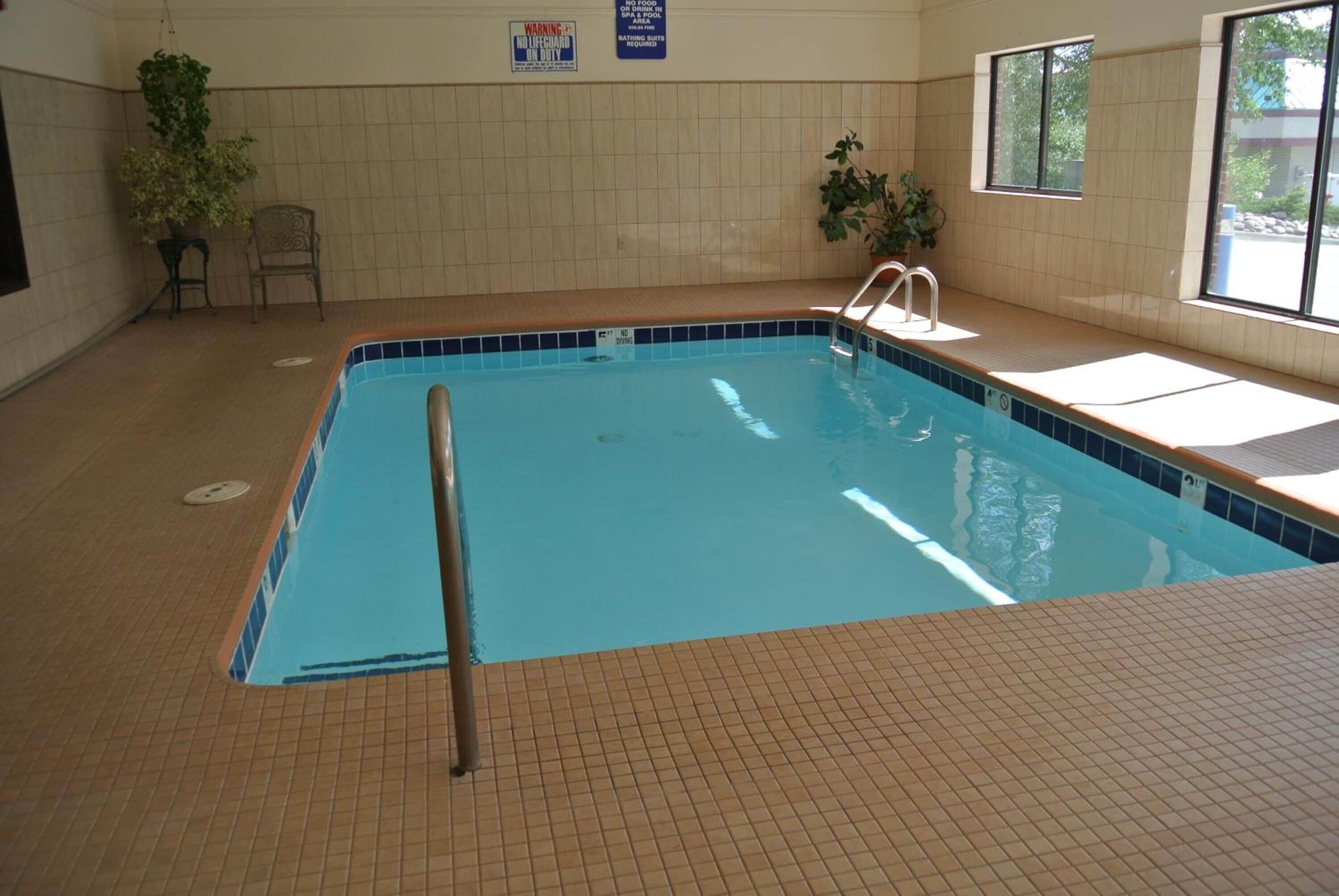 Una piscina interior con suelo de baldosas, una escalera de piscina y un ventanal que proporciona luz natural.