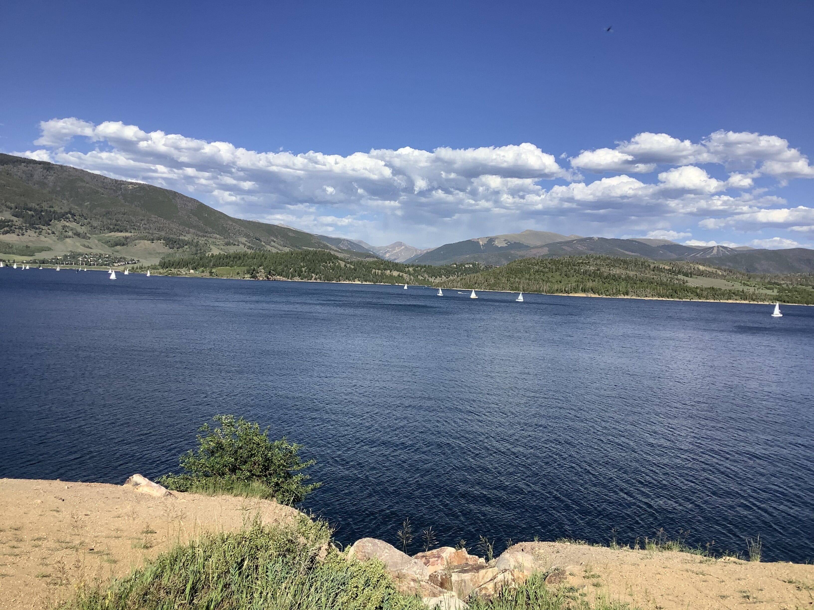 A lake with sailboats, surrounded by mountains and a clear sky.