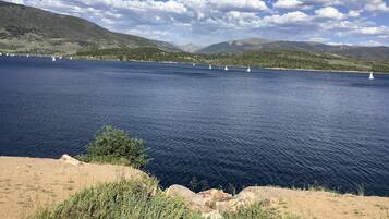 Un lago con veleros, rodeado de montañas y un cielo despejado.