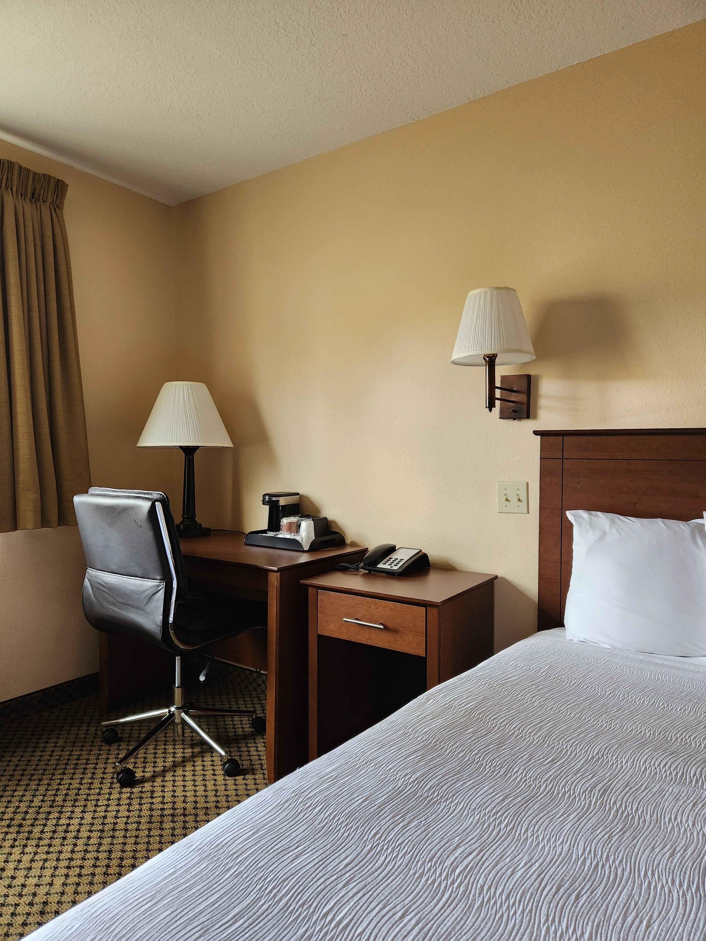 A hotel room with a bed, desk, chair, lamps, and a telephone.