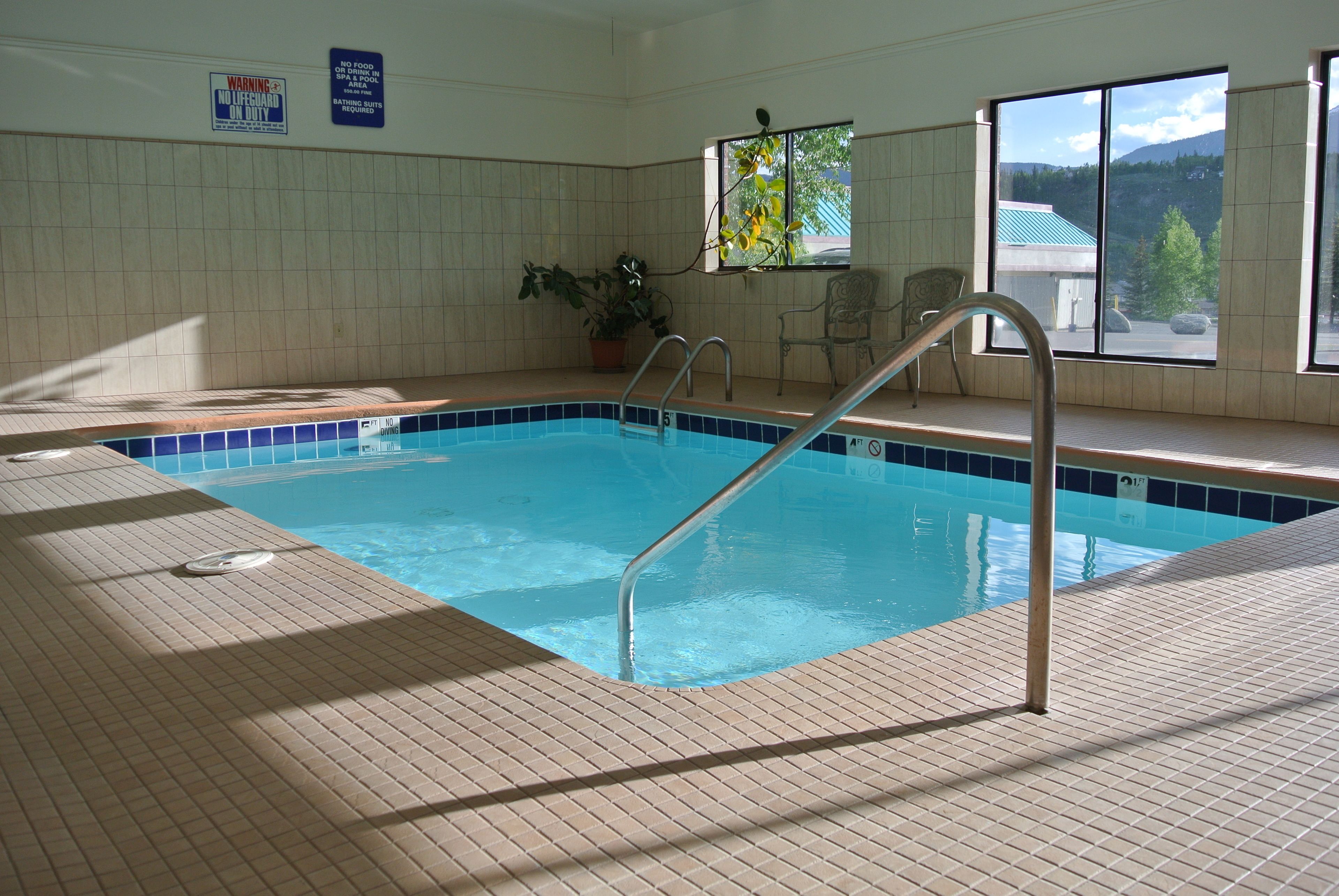 An indoor swimming pool with tiled walls, a window with a view of mountains, and a sign warning against diving.