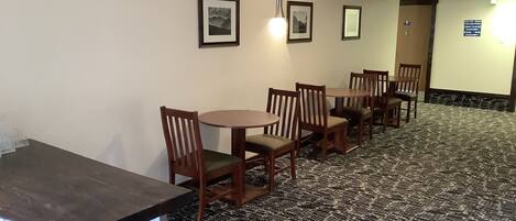 Une chambre d’hôtel dotée d’un coin repas avec des tables et des chaises en bois, une moquette à motifs et des tableaux encadrés aux murs.