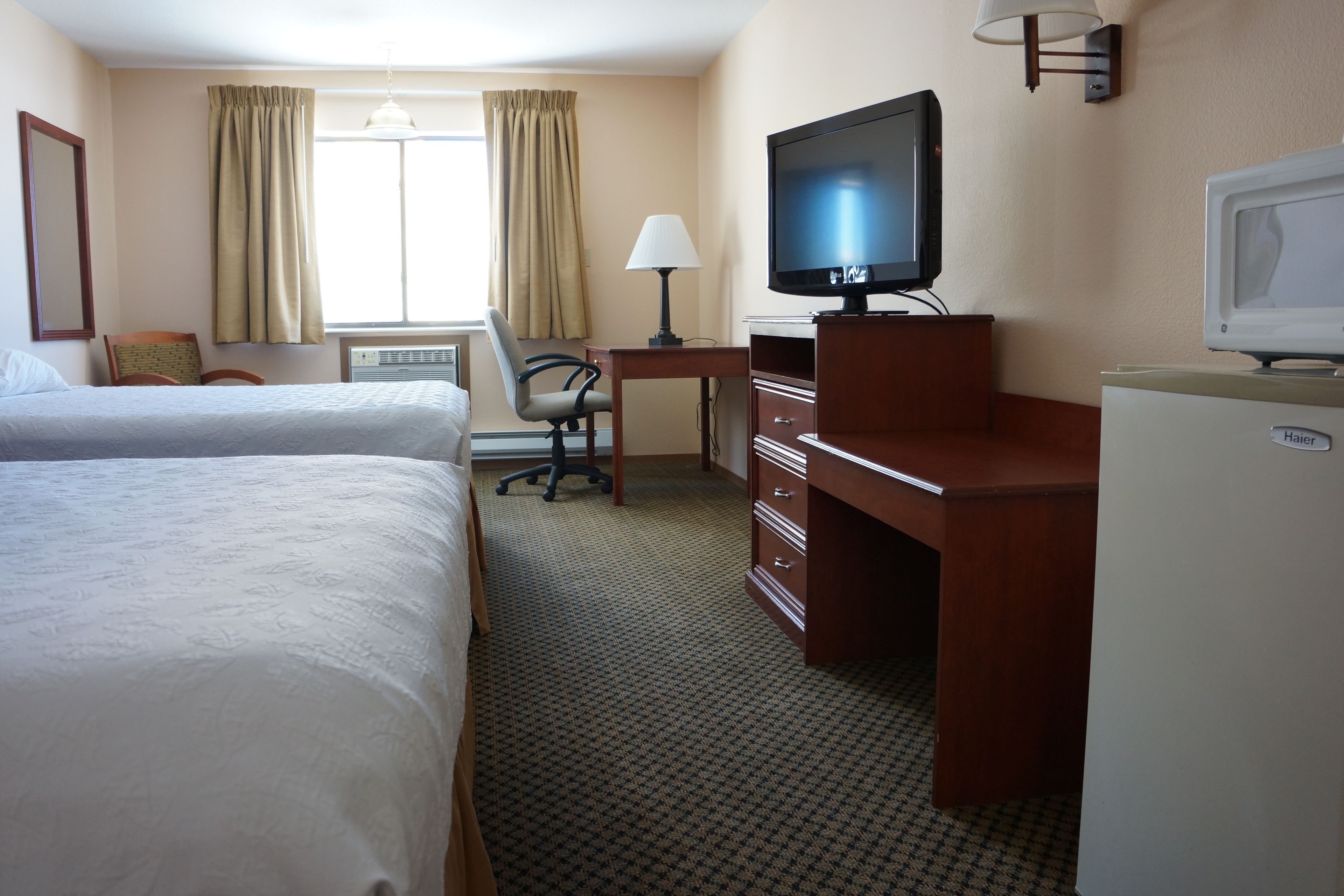 A hotel room with two beds, a desk with a television, a chair, and a refrigerator.