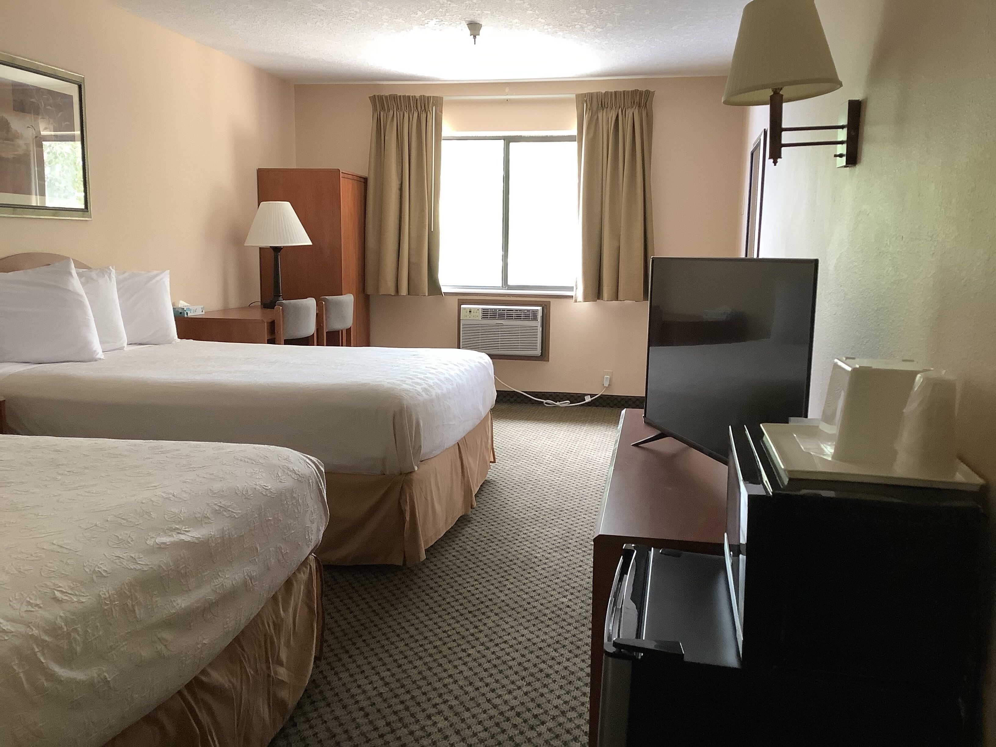 Een hotelkamer met twee bedden, een bureau met een televisie, een lamp en een raam met gordijnen.