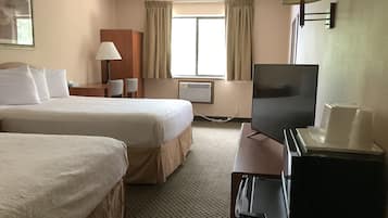 Ett hotellrum med två sängar, ett skrivbord med en tv, en lampa och ett fönster med gardiner.