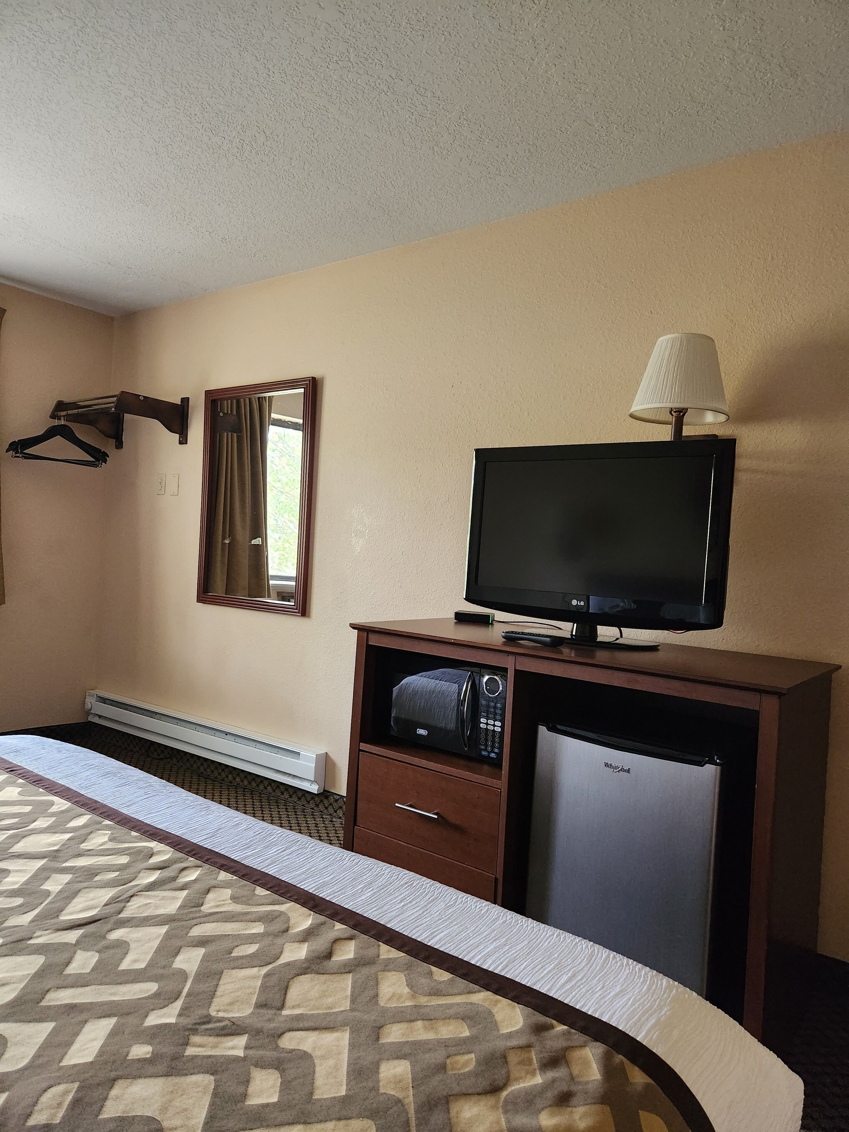 Quarto de hotel com cama, televisão, micro-ondas, frigorífico, candeeiro e cabideiro.