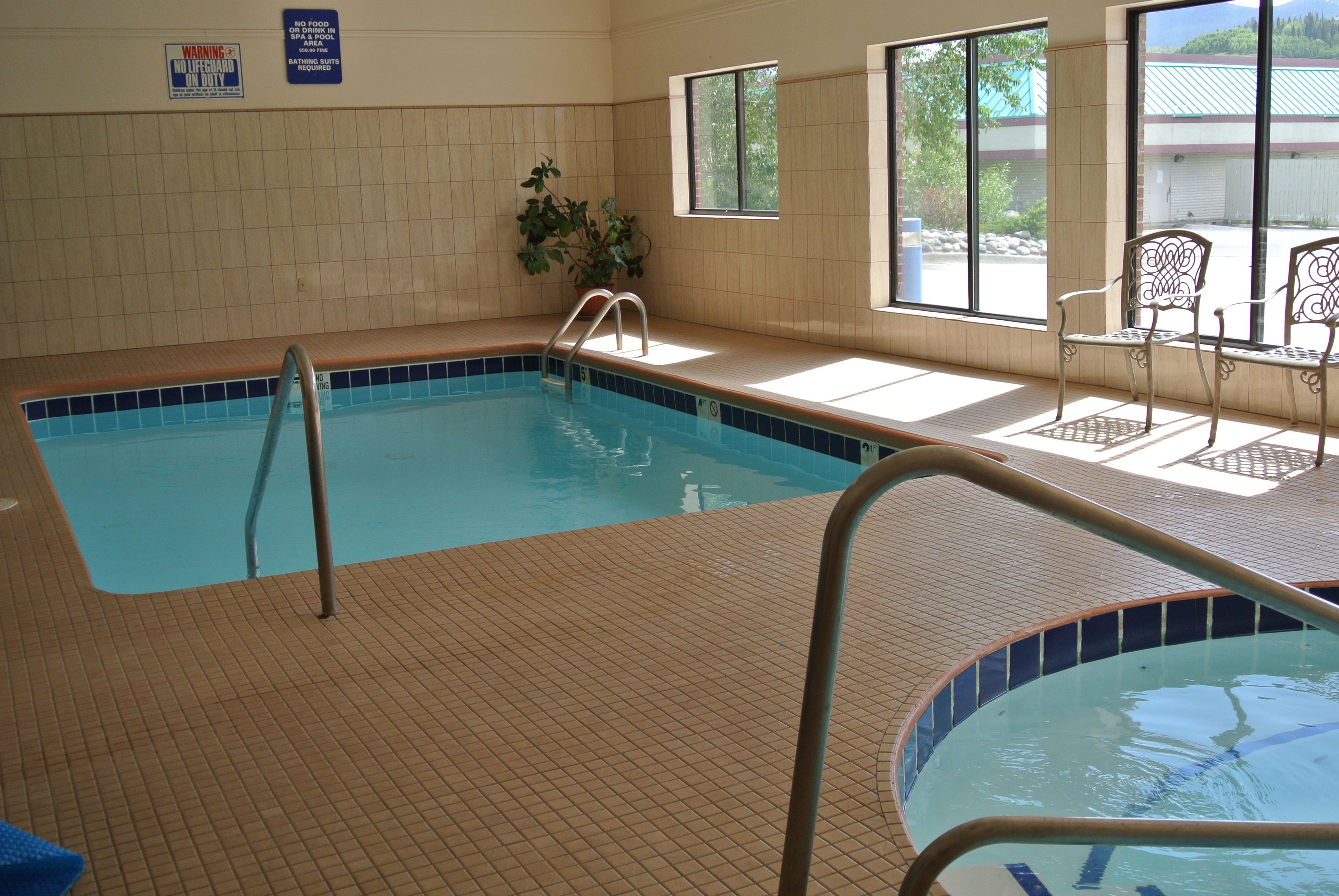 An indoor swimming pool with tiled walls and a tiled floor, a lifeguard chair, and a window with a view of the outside.