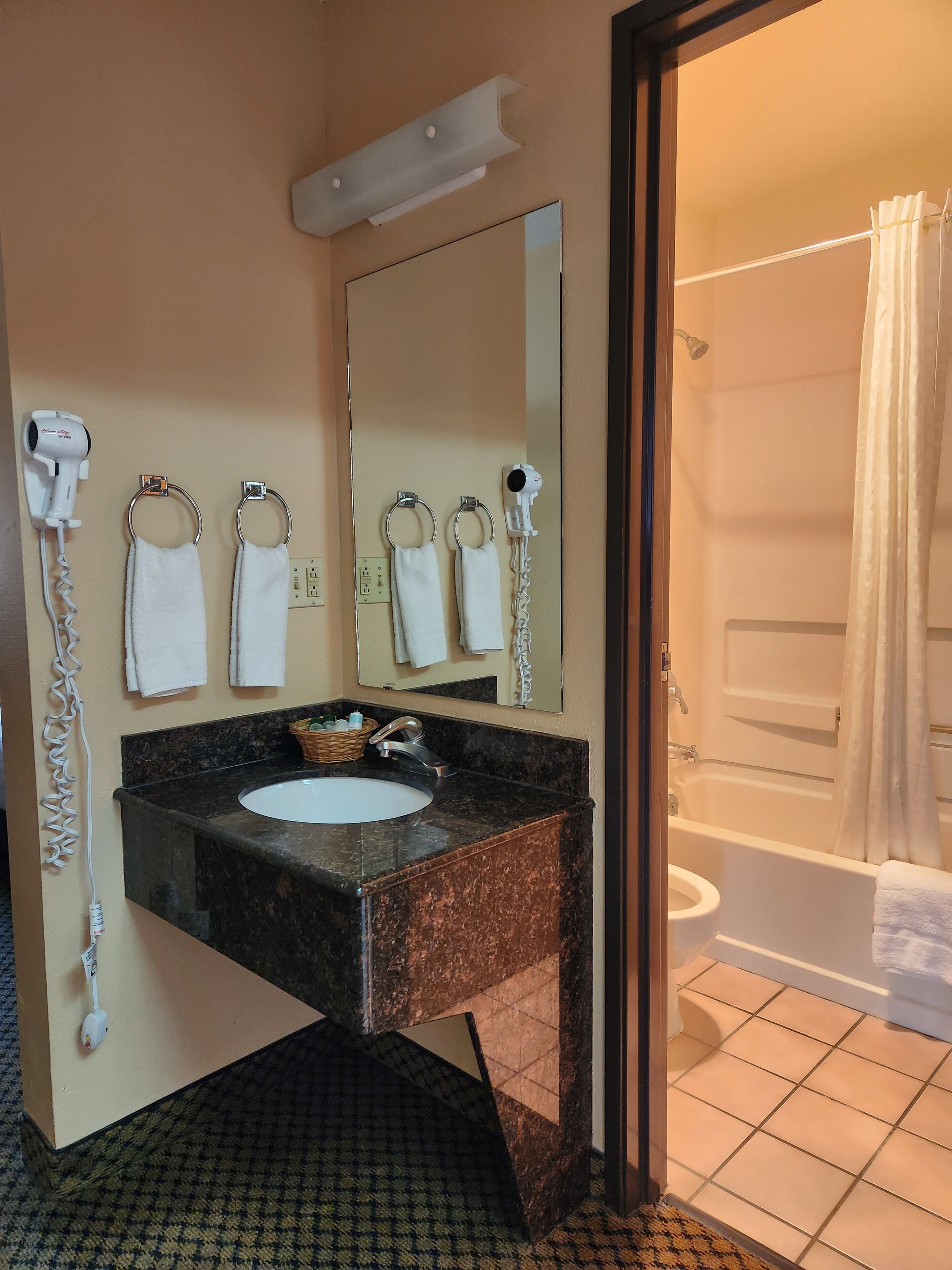 A bathroom with a sink, mirror, towel rings, and a shower area.