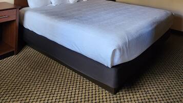 A hotel room with a large bed, two bedside tables, a nightstand, a wall-mounted lamp, and a framed picture.