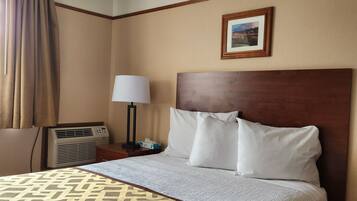 A hotel room with a large bed, a headboard, a bedside table with a lamp, a picture on the wall, and an air conditioning unit.
