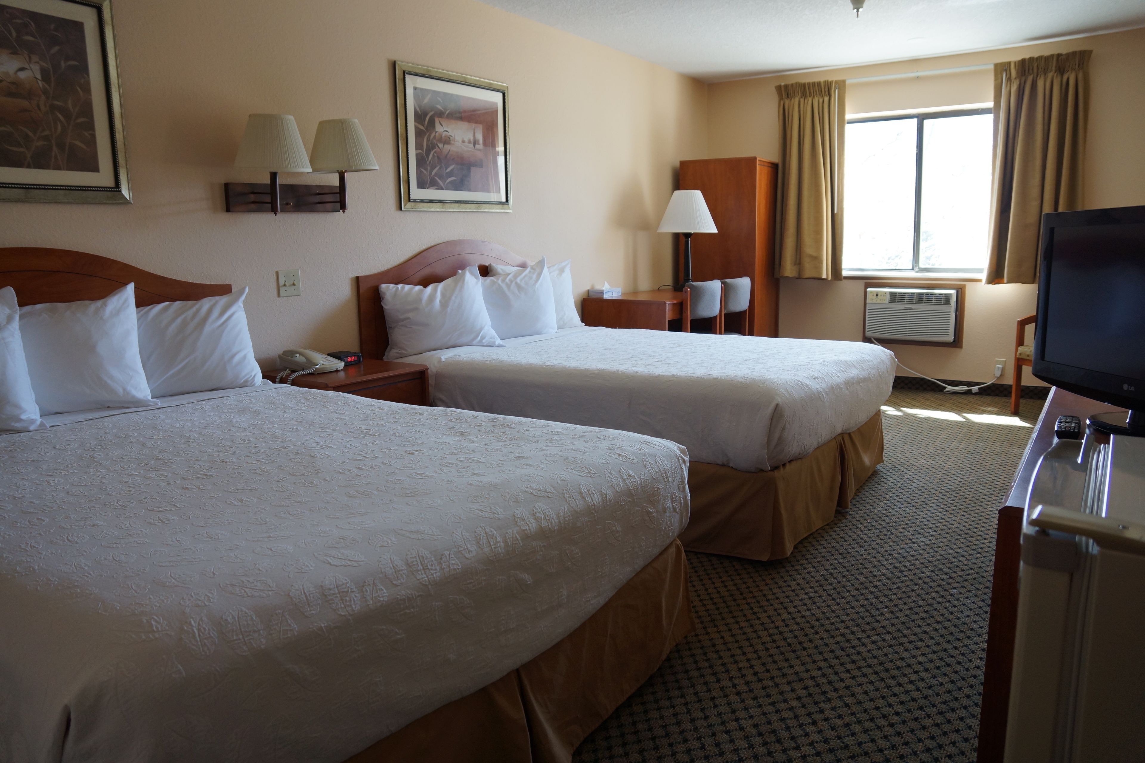 A hotel room with two beds, a desk with a lamp, a television, and a window with curtains.