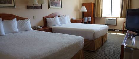 A hotel room with two beds, a desk with a lamp, a television, and a window with curtains.