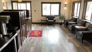 A lobby with wooden flooring, a reception desk, a coffee machine, and seating areas with chairs and a sofa.