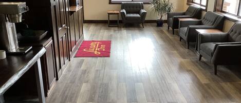 Un vestíbulo con piso de madera, una recepción, una máquina de café y zonas de estar con sillas y un sofá.