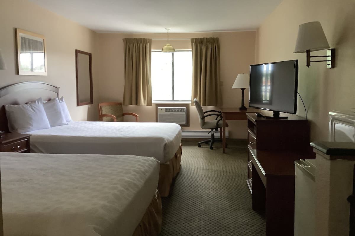A hotel room with two beds, a desk with a television, a chair, and a lamp.