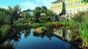 Una vista serena de un lago con un edificio amarillo, rodeado de exuberante vegetación y una masa de agua tranquila que refleja el cielo.