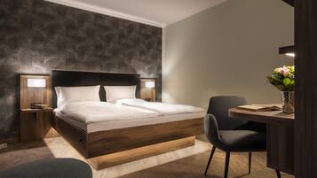 A modern bedroom with a wooden bed, bedside lamps, a desk, and a chair.
