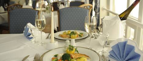 Una mesa de comedor dispuesta con platos de comida, copas de vino y cubiertos.