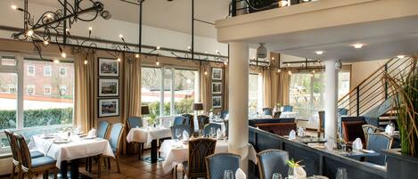 A restaurant with multiple dining tables, chairs, and a staircase leading to an upper level.