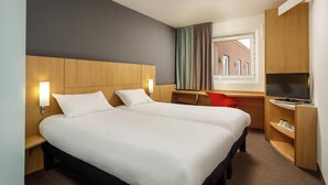 Una habitación de hotel con una cama grande, un escritorio, un televisor y una ventana con cortinas.