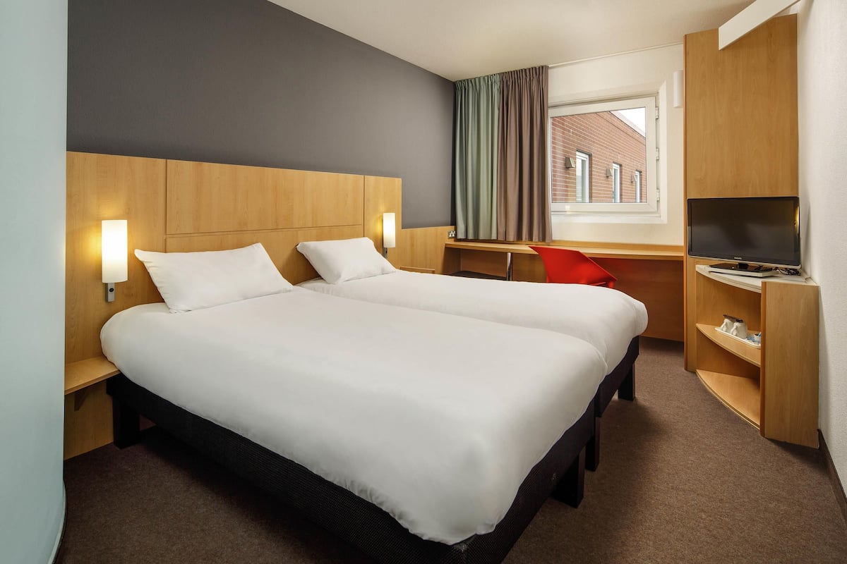 A hotel room with a large bed, a desk, a TV, and a window with curtains.
