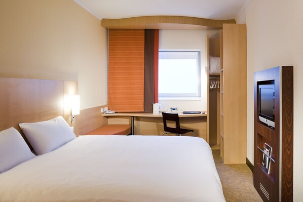 A hotel room with a large bed, a desk with a chair, a television, and a window with blinds. - Ibis Hull City Centre (Hull)