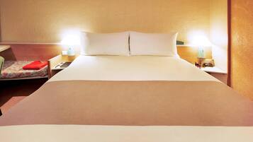 A neatly made bed with white linens, a red pillow, and two bedside lamps.