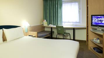 Habitación de hotel con cama, escritorio, silla, televisor y ventana con cortinas.