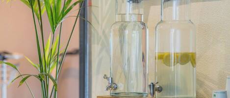 Two glass bottles with cork stoppers on a wooden cabinet, one containing a clear liquid with a slice of lemon, and a potted plant beside them.