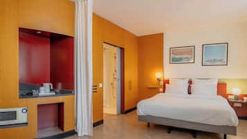 A hotel room with a bed, a desk with a microwave, a shower, and two framed pictures on the wall.