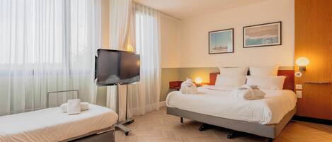 A hotel room with two beds, a TV, and a large window with sheer curtains.