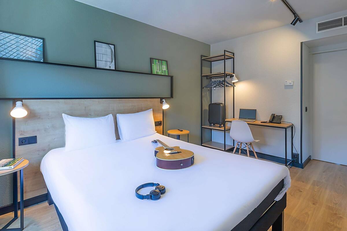 Een moderne hotelkamer met een groot bed, een bureau met een laptop, een gitaar en een kapstok.