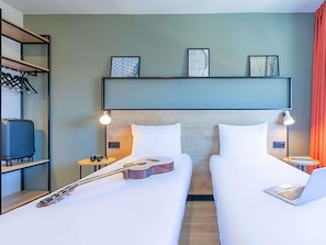 Ein Hotelzimmer mit zwei Betten, einer Gitarre, einem Koffer und einem Laptop.