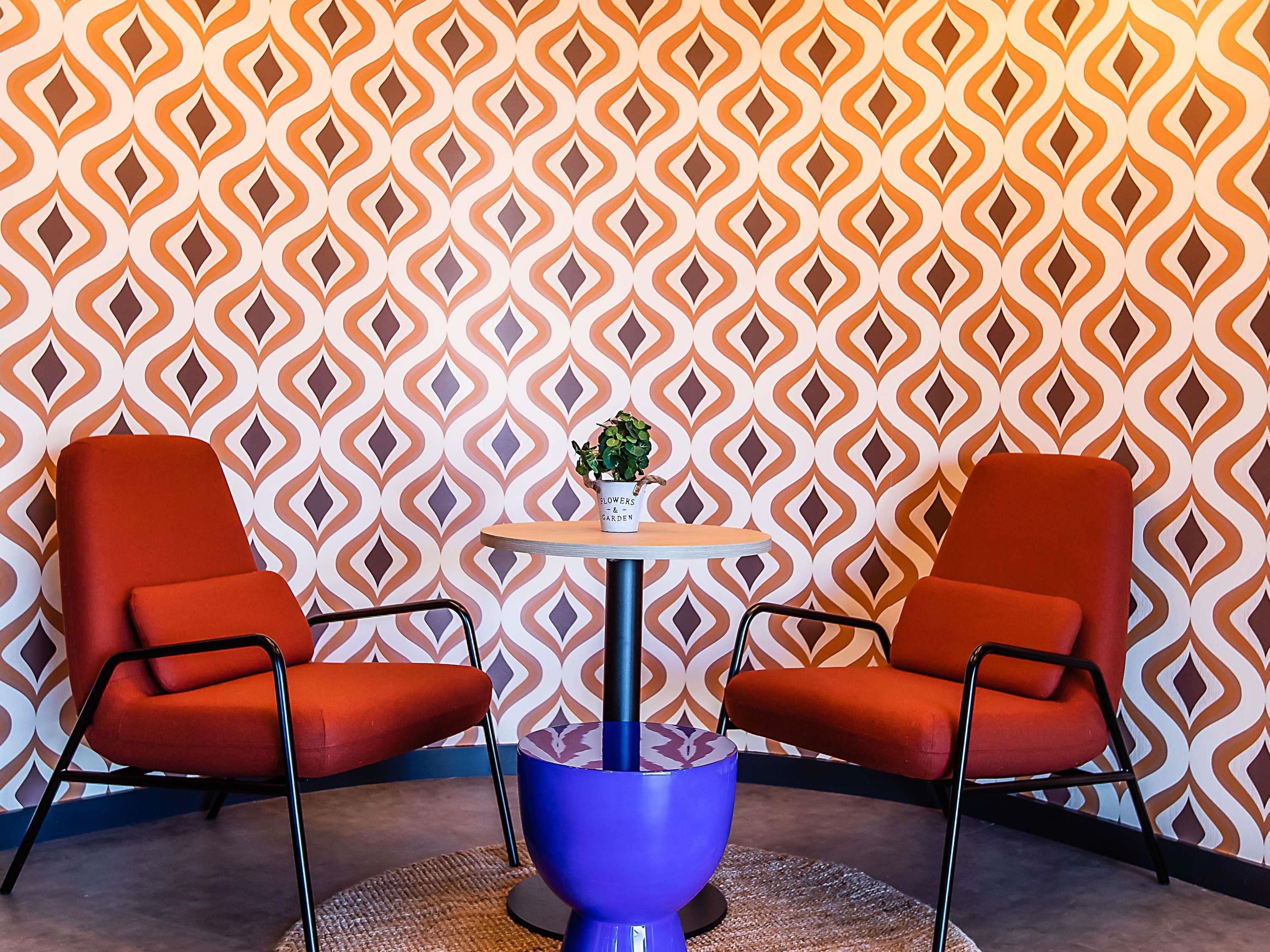 Una habitación con dos sillas rojas, una mesa redonda pequeña con base azul y una planta en maceta sobre la mesa.