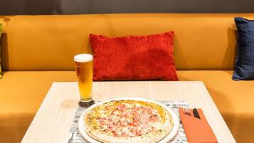 Pizza sobre una mesa cubierta con periódico, una jarra de cerveza y un cojín rojo en un sofá amarillo.