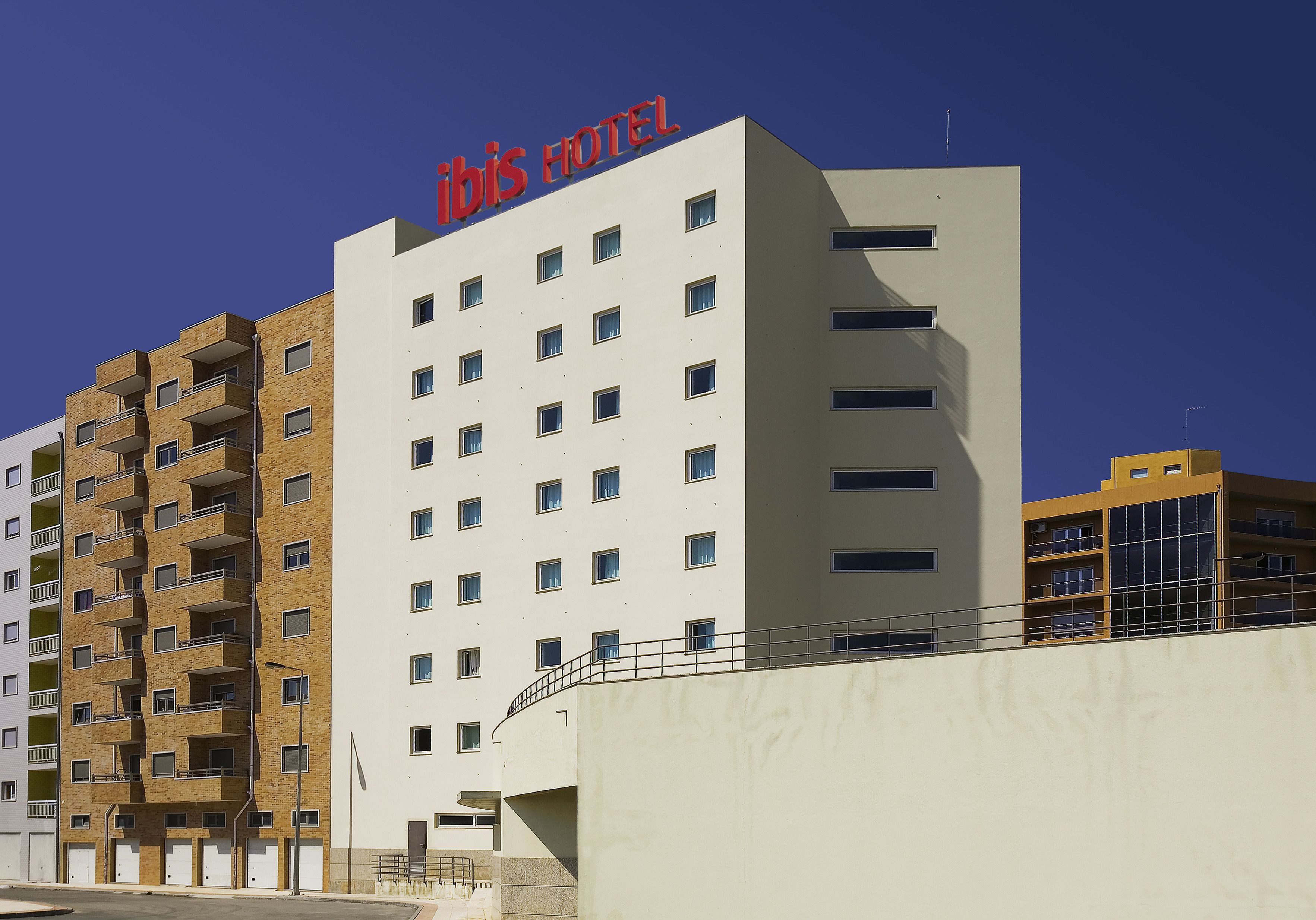 A multi-story hotel with a prominent "ibis HOTEL" sign, featuring a modern architectural design with balconies and a flat facade.