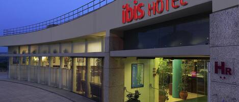 The exterior of ibis hotel with a modern design, featuring a prominent signage and a glass entrance.