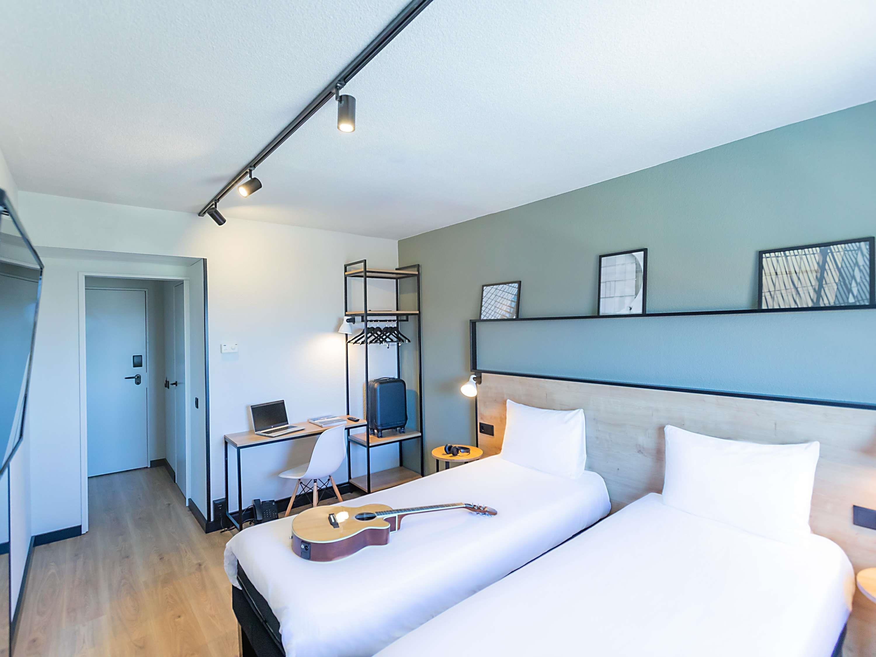 Een hotelkamer met een bed, een bureau met een laptop, een gitaar, een koffer en een kledingkast.