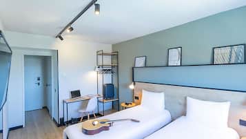 Een hotelkamer met een bed, een bureau met een laptop, een gitaar, een koffer en een kledingkast.