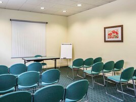 Un salón de conferencias con una pizarra, pantalla de proyector y sillas verdes dispuestas alrededor de una mesa.
