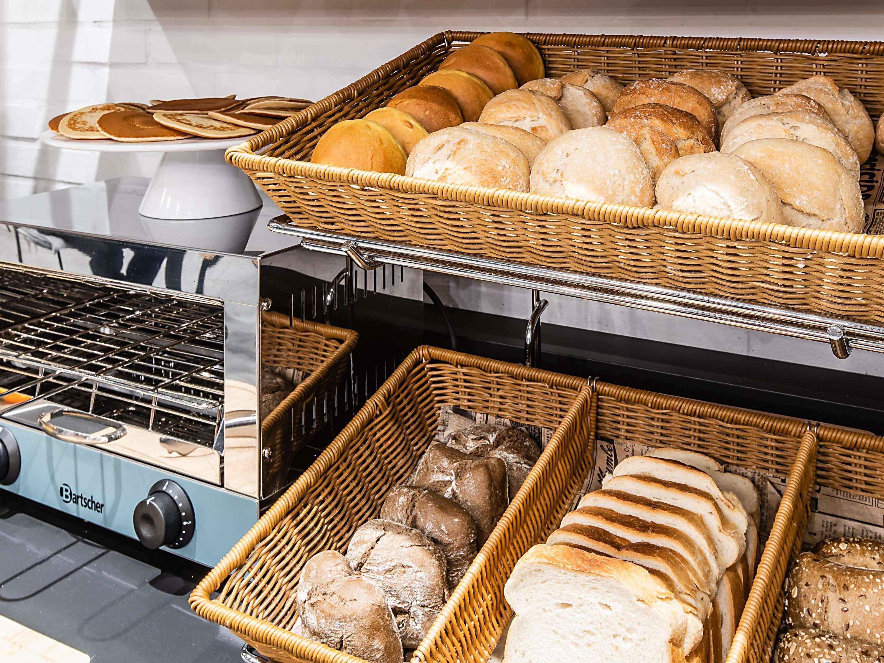 A kitchen area with a Bartscher stove, wicker baskets filled with various breads, and a white countertop.