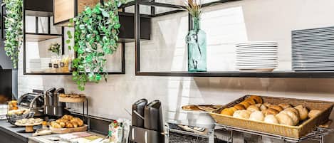 A buffet setup with various food items, a coffee machine, and decorative plants.