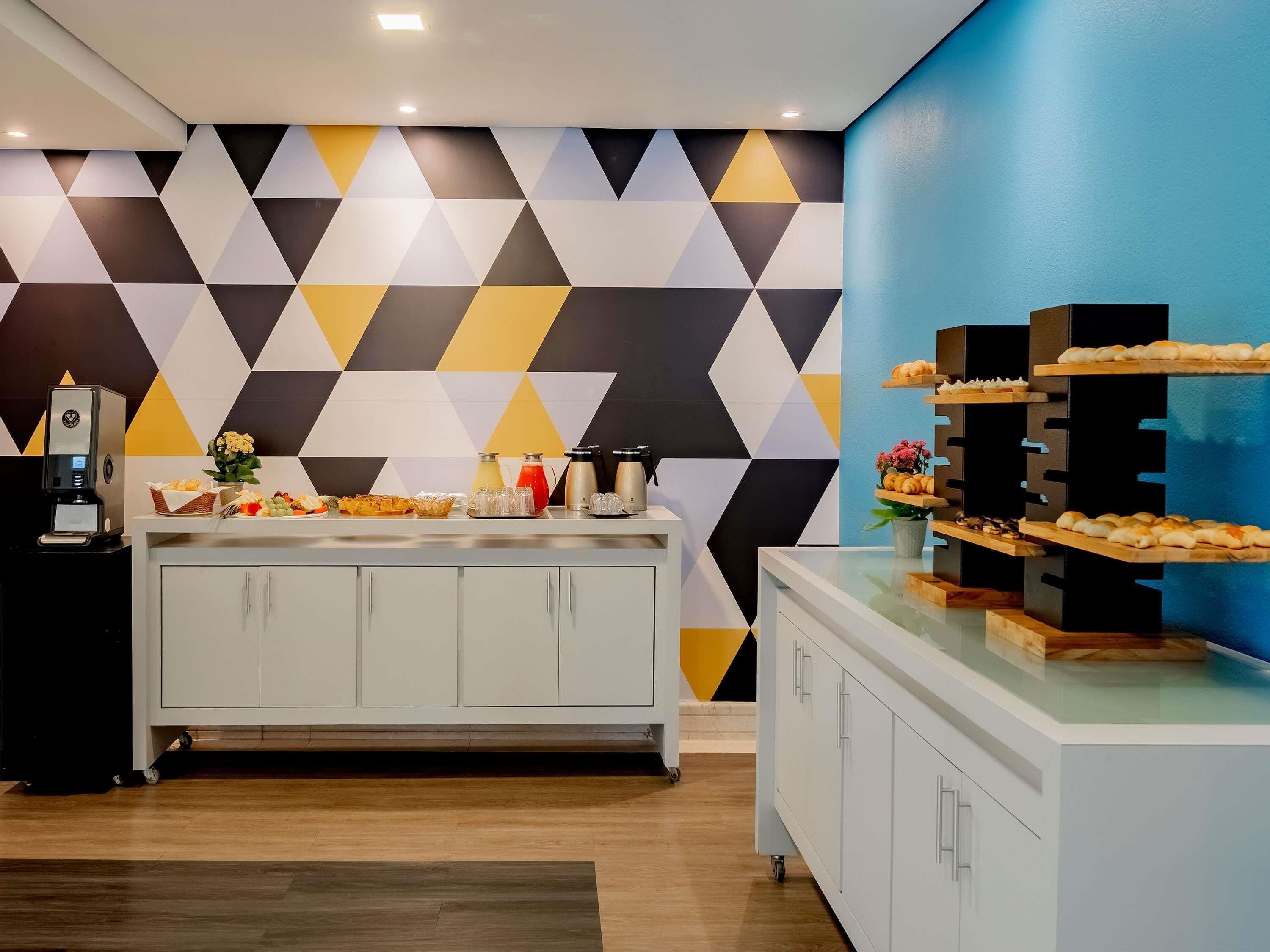 A modern kitchen with a geometric-patterned wall, a coffee station, and a display of pastries.