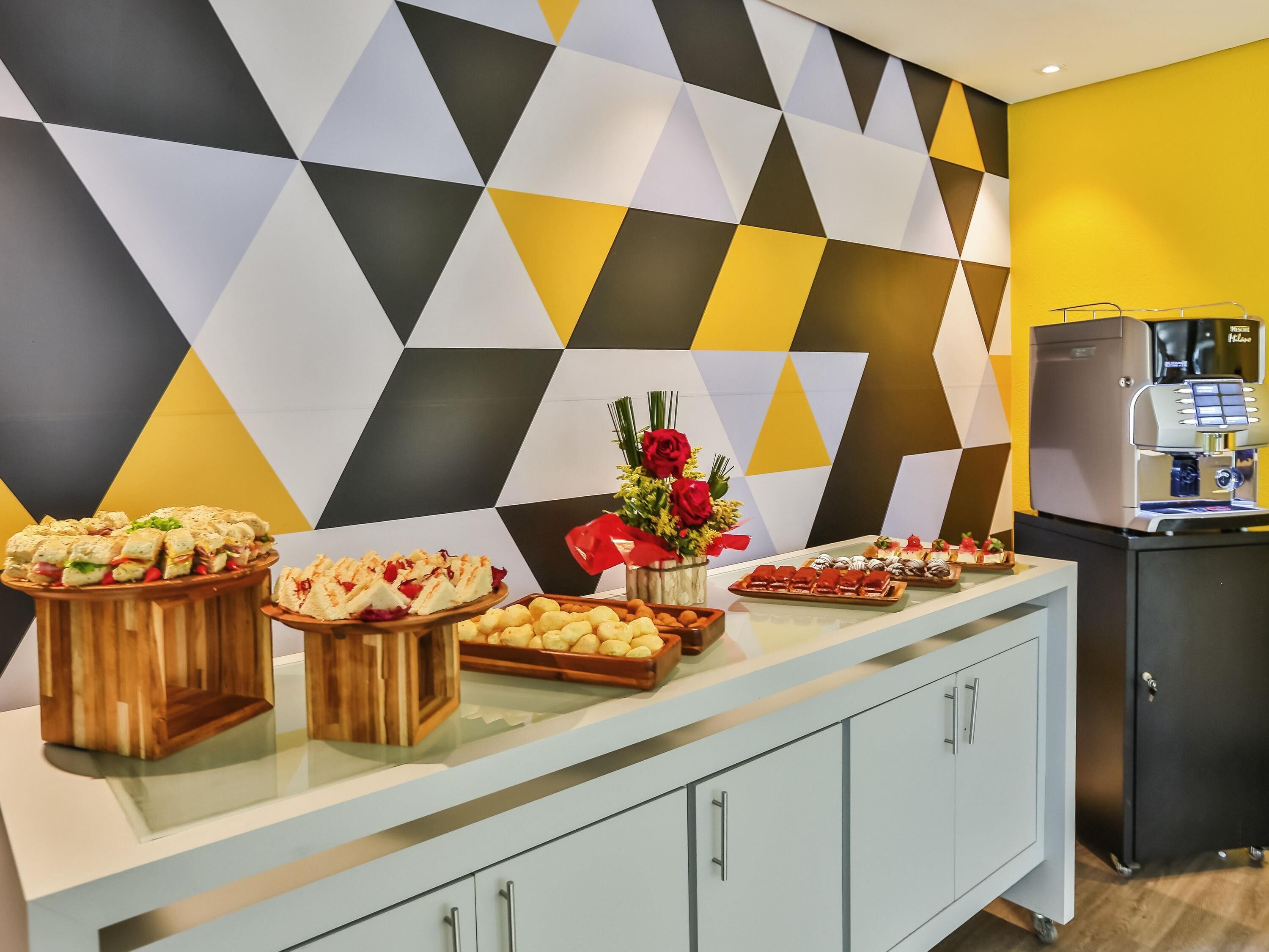 A buffet setup with various food items, a coffee machine, and a decorative vase with flowers.