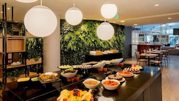 A modern restaurant with a buffet setup, featuring a variety of dishes and a green leafy wall backdrop.