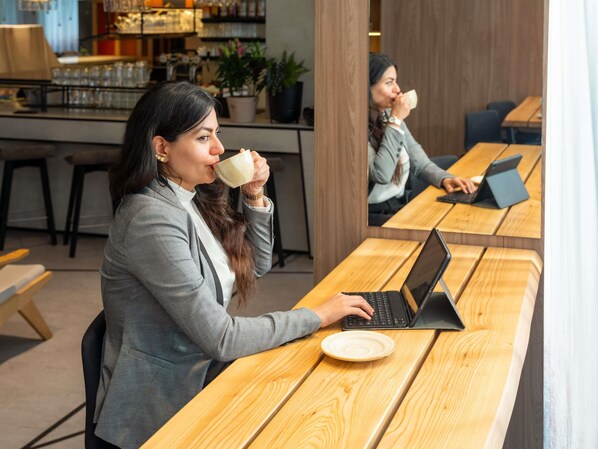 A person sitting at a wooden table with a laptop, holding a cup. - Novotel Suites Wien City Donau (Vienna)