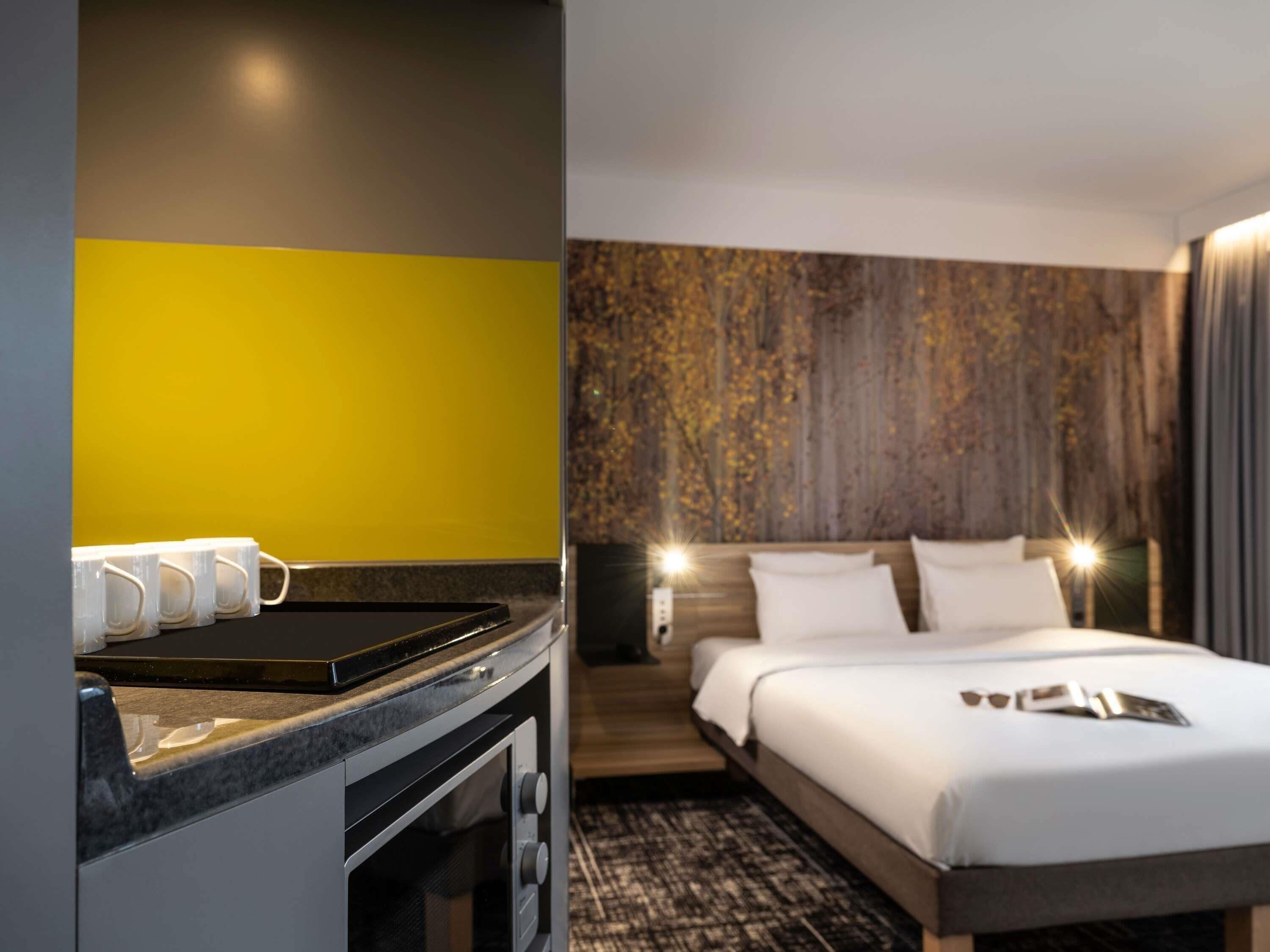 A hotel room with a bed, bedside lamps, a coffee machine, and a wall with a textured pattern.