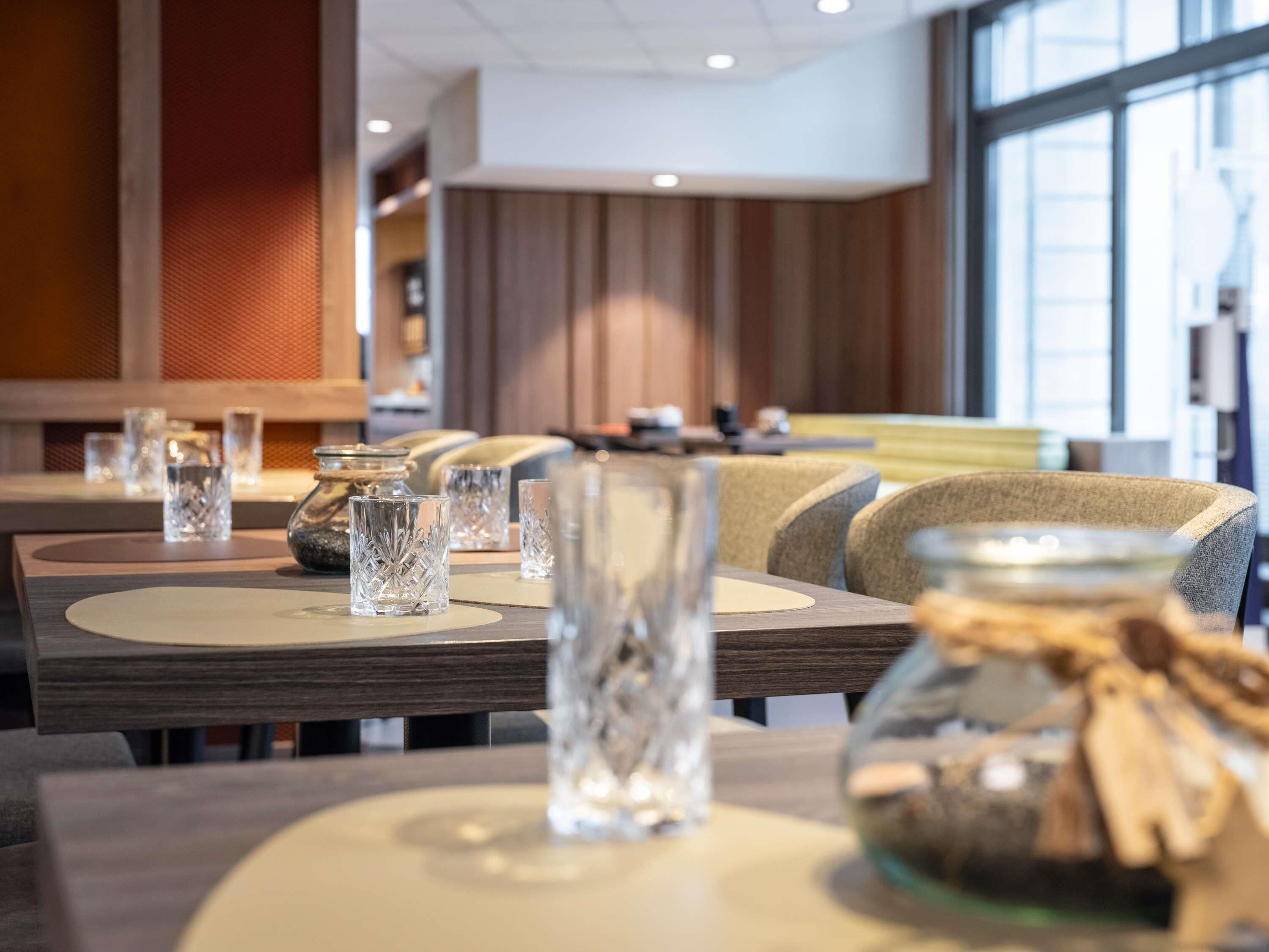 A restaurant interior with tables set for dining, featuring clear glassware and decorative jars.